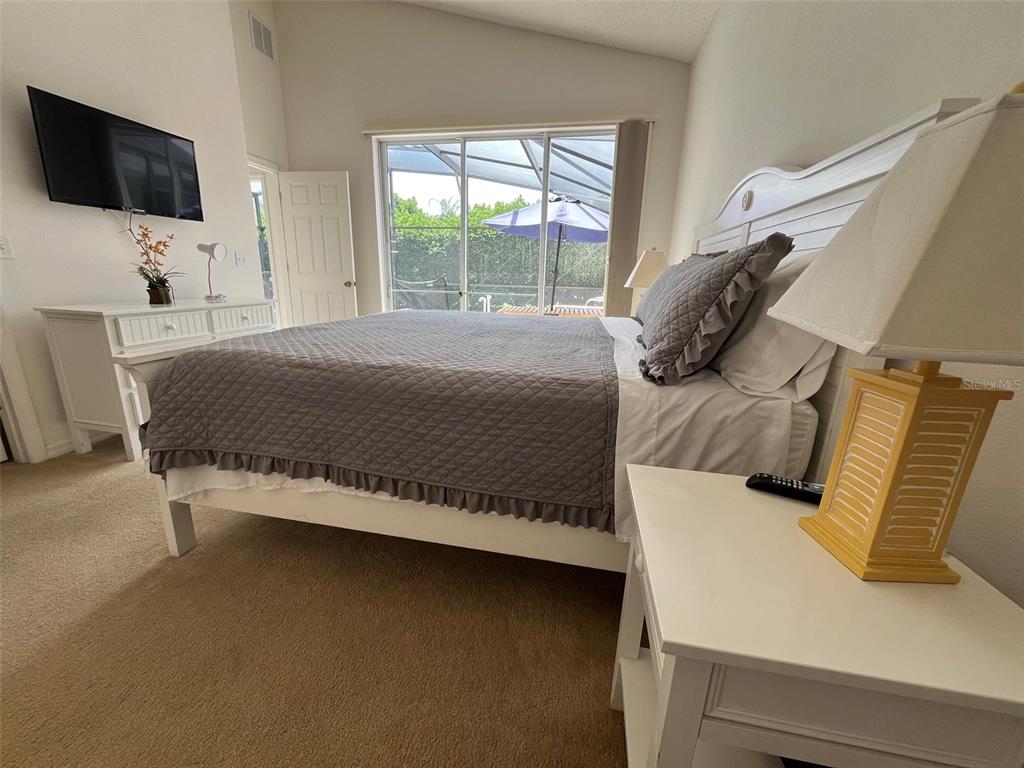 A bedroom features a white bed frame, a gray quilt, and a view of a pool — 16628 FRESH MEADOW DRIVE, CLERMONT, FL