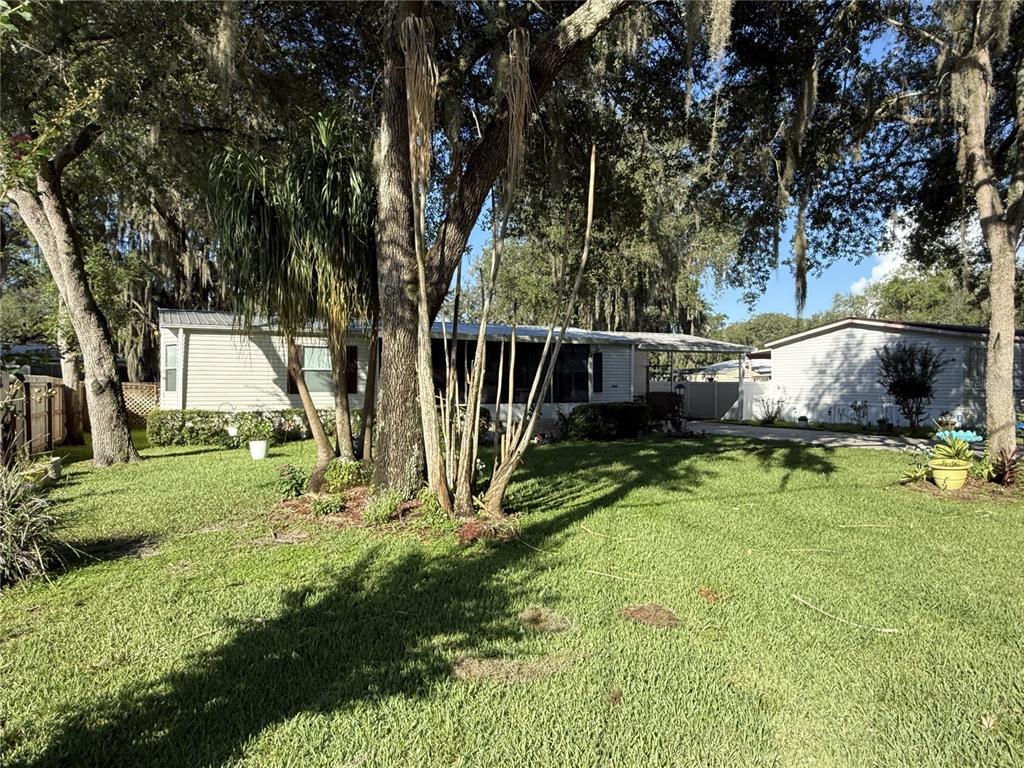 A single-story manufactured home with a carport sits on a grassy lot with mature trees — 8634 TREASURE ISLAND ROAD, LEESBURG, FL