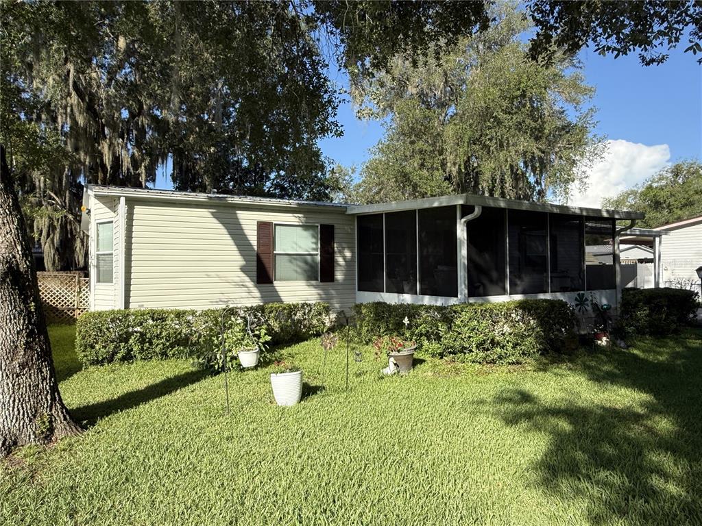A single-story mobile home with beige siding and a screened-in porch sits on a lawn — 8634 TREASURE ISLAND ROAD, LEESBURG, FL