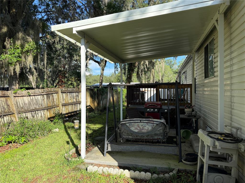 A covered concrete patio features a porch swing, a grill, and a wooden deck nearby — 8634 TREASURE ISLAND ROAD, LEESBURG, FL