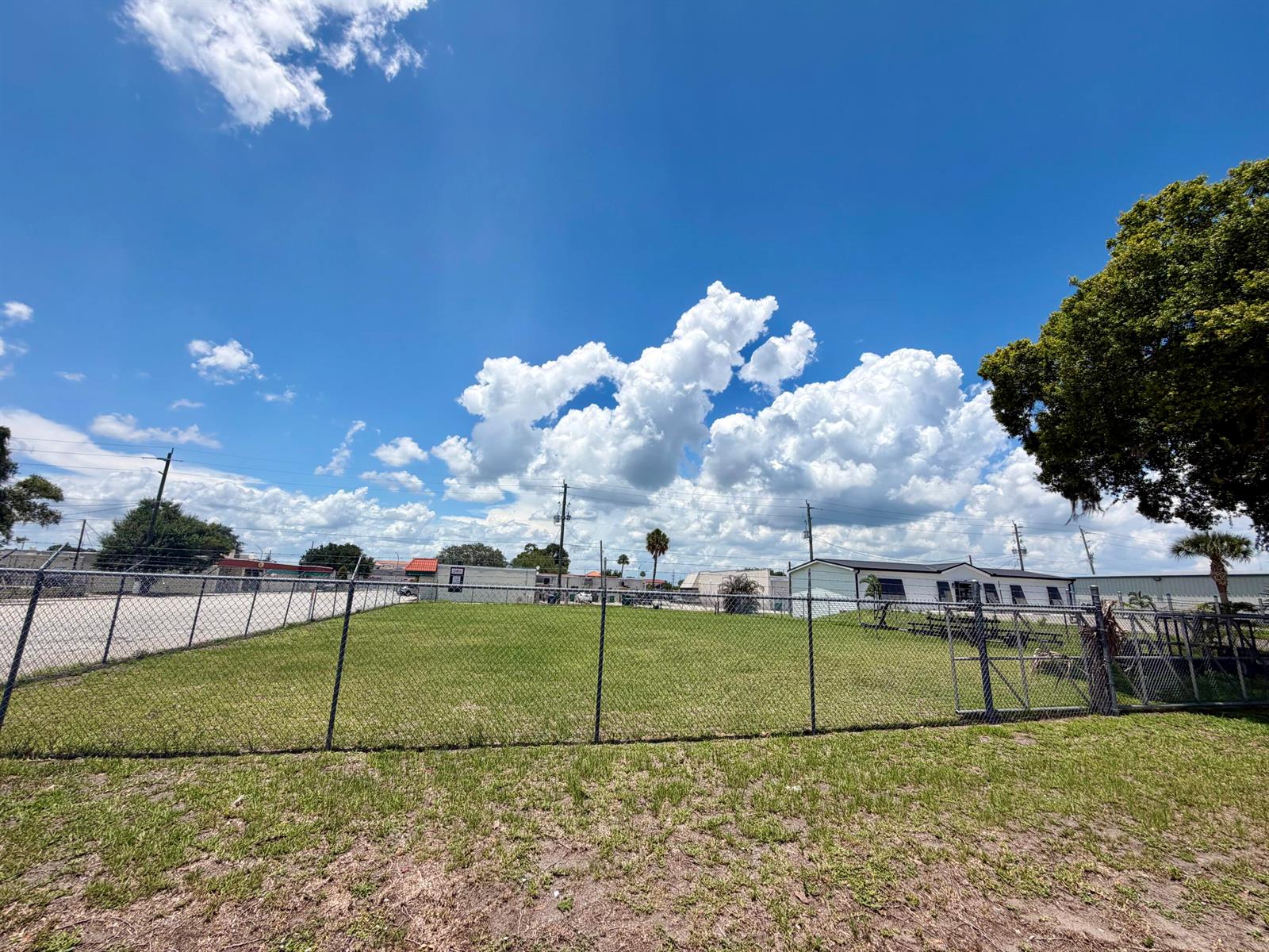 A fenced, grassy lot sits under a bright blue sky with large white clouds — 203 SW 3rd Avenue, Okeechobee FL 34974, OKEECHOBEE, FL