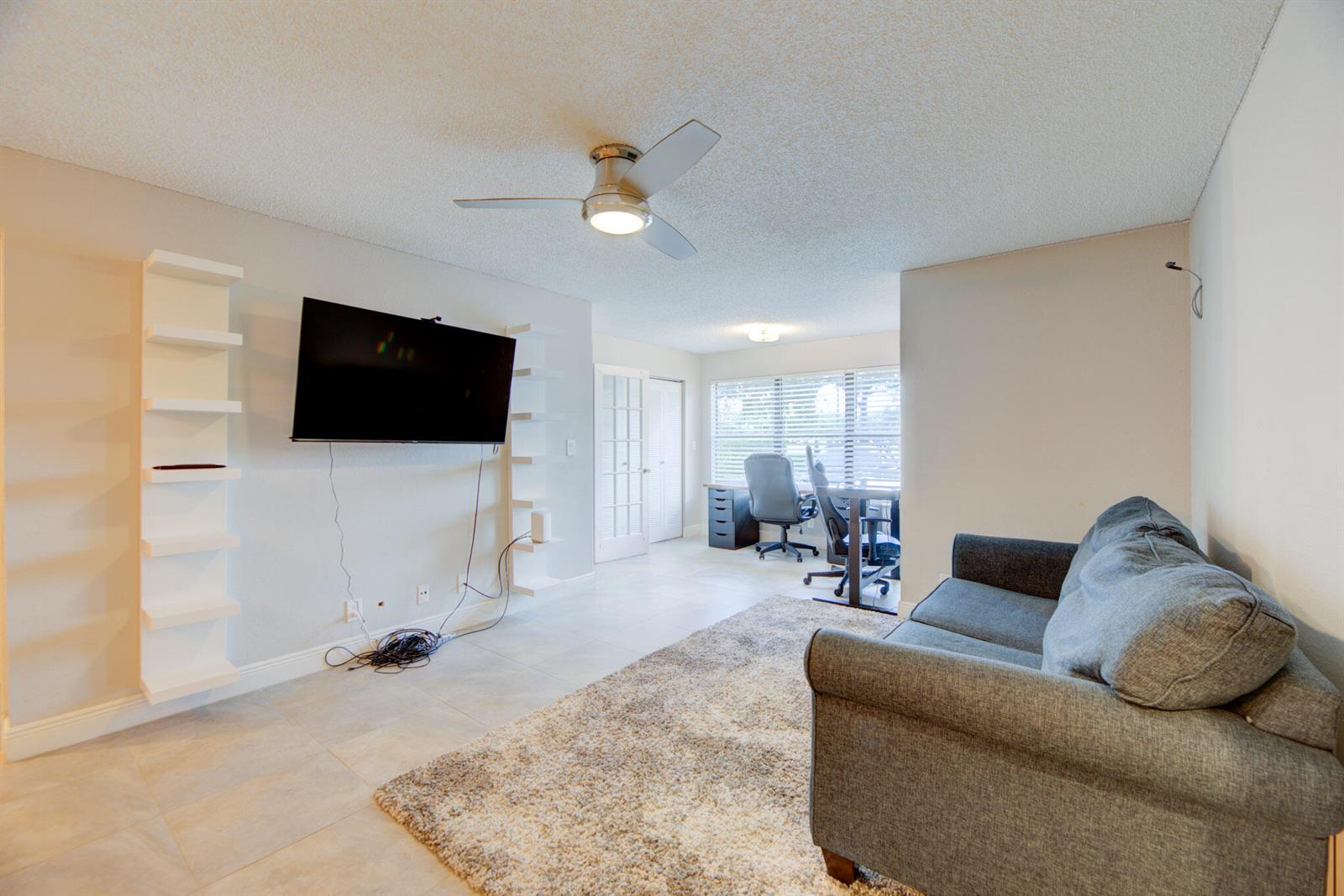 A living room features a wall-mounted television, white shelving, a gray sofa, and a desk — 2900 S University Drive # 9104, Davie FL 33328, DAVIE, FL