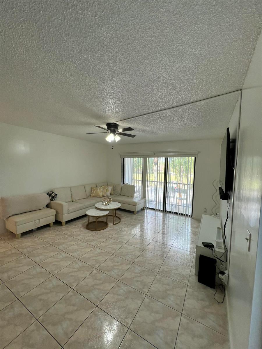 A living room with tile flooring, a sectional sofa, a ceiling fan, and sliding glass doors — 1007 Green Pine Boulevard # D2, West Palm Beach FL 33409, WEST PALM BEACH, FL
