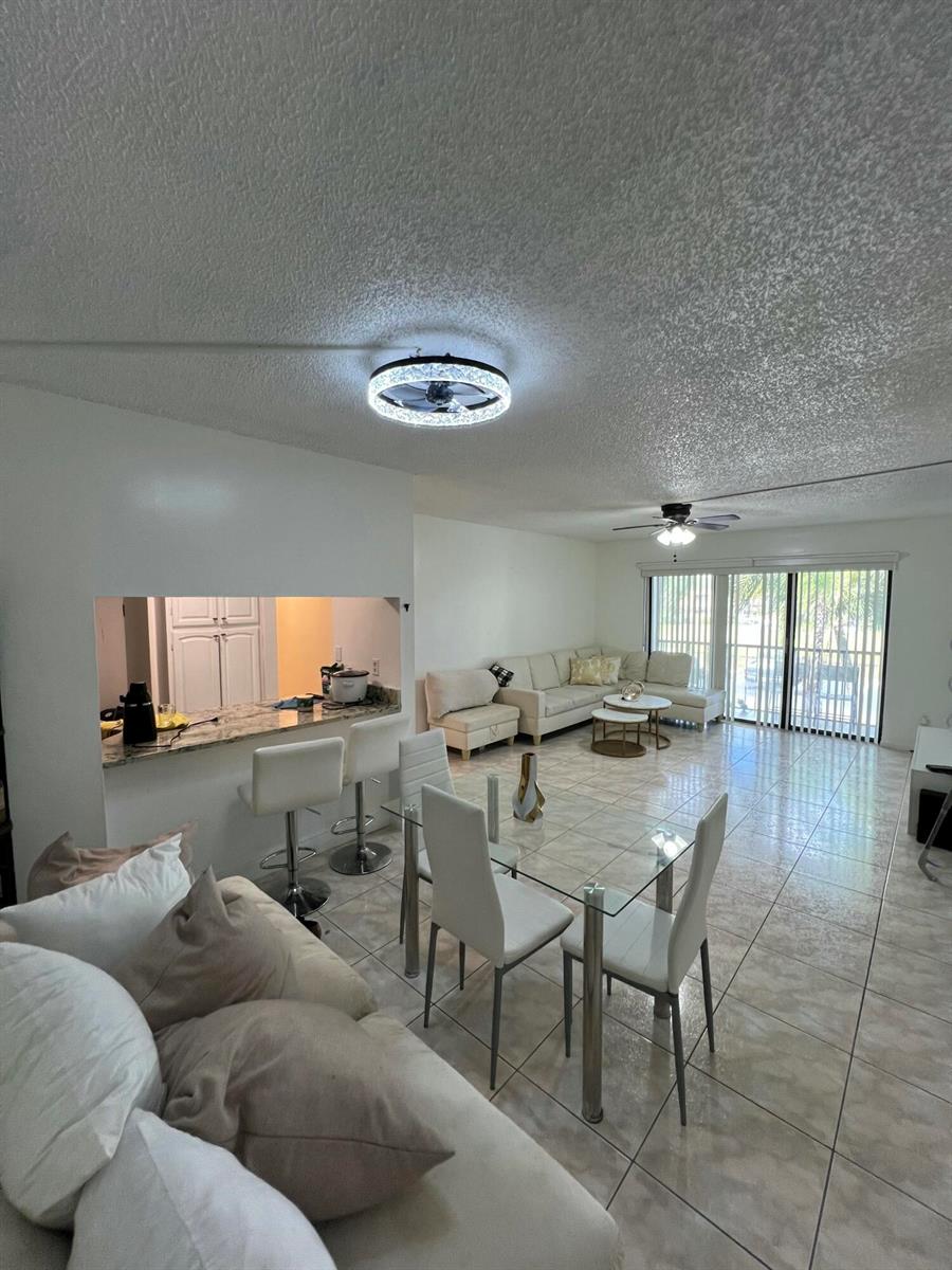 An open-concept living and dining area features tile flooring, white furniture, and a kitchen pass-through — 1007 Green Pine Boulevard # D2, West Palm Beach FL 33409, WEST PALM BEACH, FL