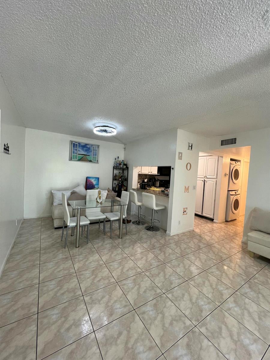 An open-concept living and dining area features tile flooring, a breakfast bar, and laundry appliances — 1007 Green Pine Boulevard # D2, West Palm Beach FL 33409, WEST PALM BEACH, FL