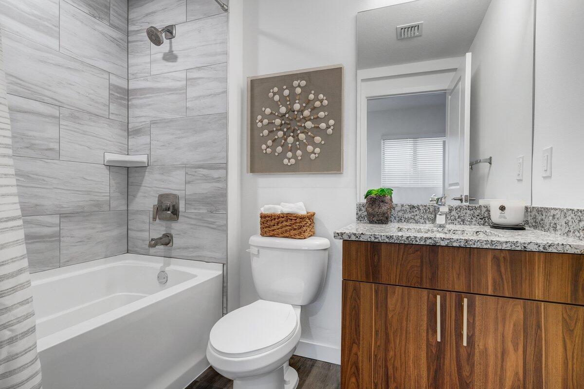 A bathroom features a wood-grain vanity, granite countertop, toilet, and a tiled shower-tub combination — 4290 Lakewood Road Unit 107, FL 33461, FL