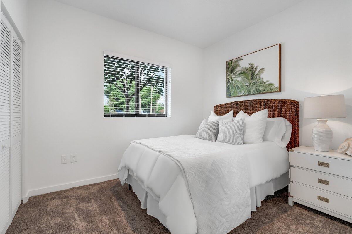 A bedroom features a bed with a woven headboard, white bedding, and a white nightstand — 4290 Lakewood Road Unit 107, FL 33461, FL