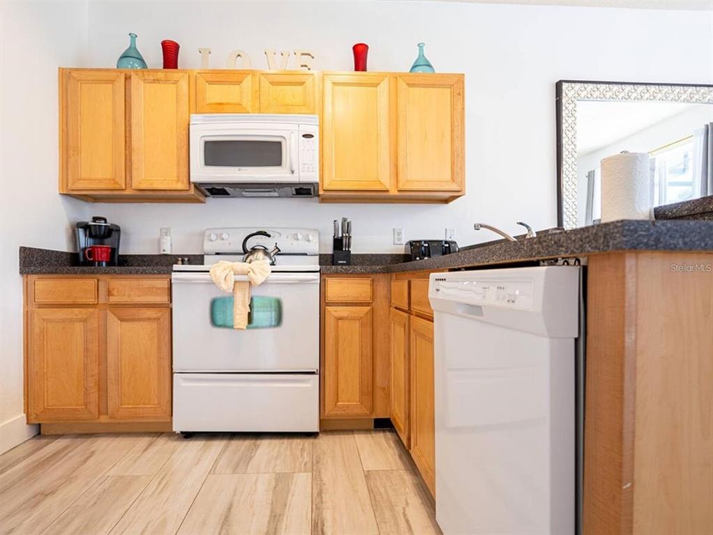 A kitchen features light wood cabinets, white appliances, dark countertops, and wood-look flooring — 540 SANDY RIDGE DRIVE, DAVENPORT, FL