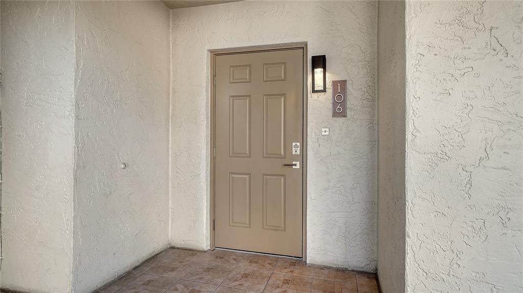 A tan six-panel front door with a digital lock is set in a stucco entryway — 4835 GULF OF MEXICO DRIVE UNIT 106, LONGBOAT KEY, FL