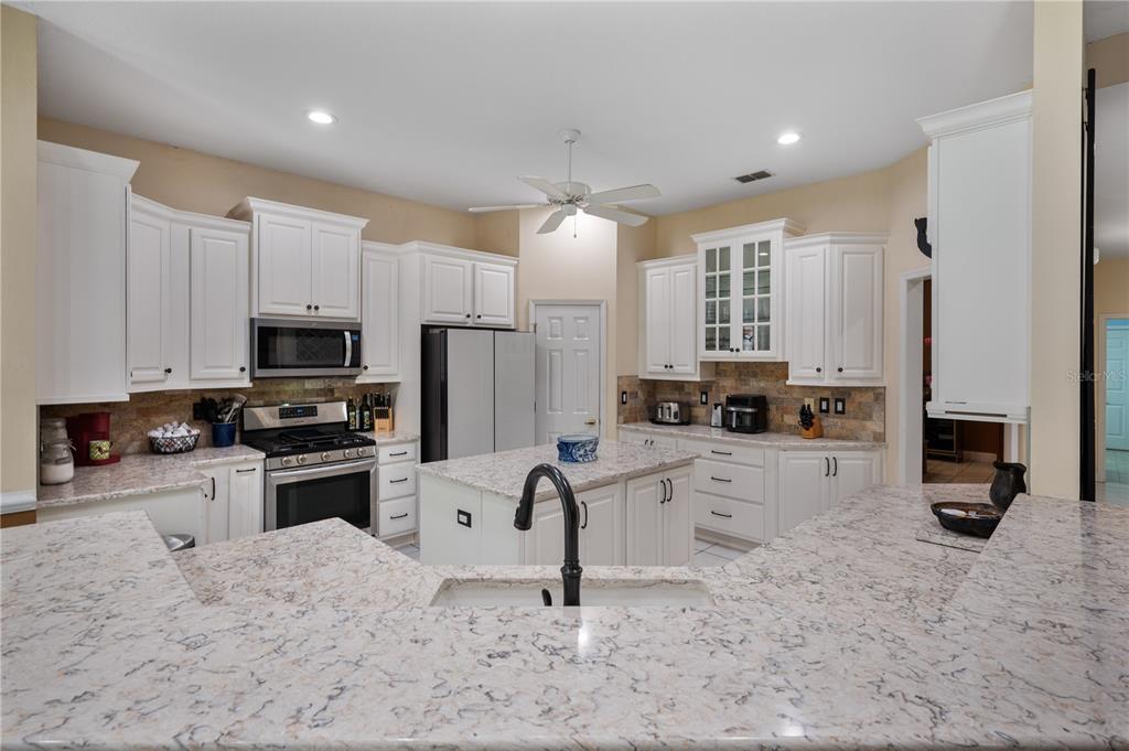 A kitchen features white cabinetry, granite countertops, a center island, and stainless steel appliances — 6617 POLEY CREEK DRIVE W, LAKELAND, FL
