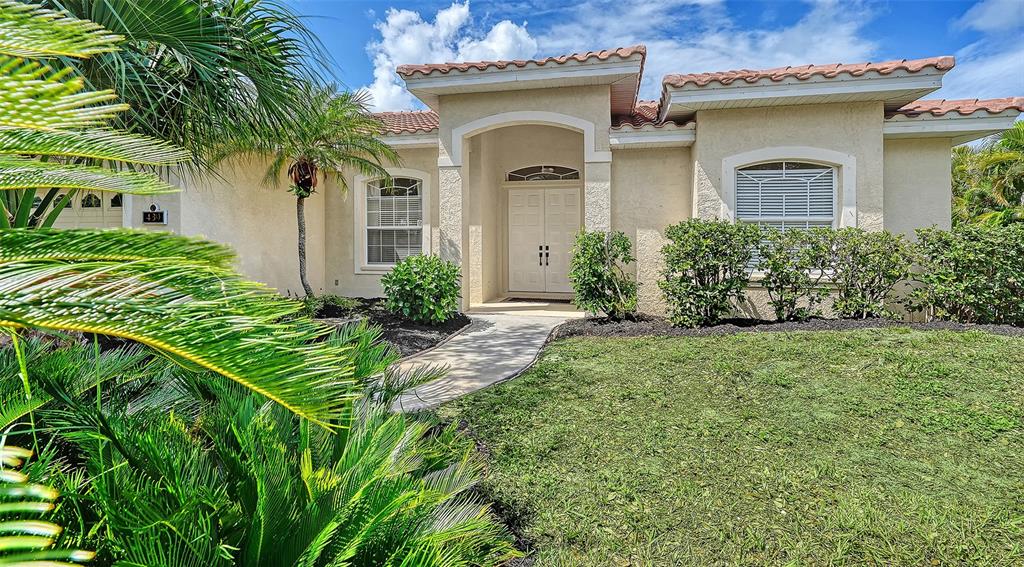 A single-story stucco house with a tiled roof, arched entryway, and landscaped front yard — 439 E ROSSETTI DRIVE, NOKOMIS, FL