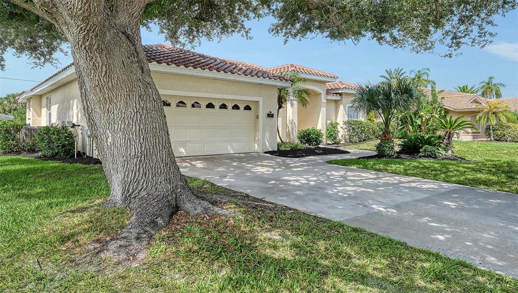 A single-story house with a beige stucco exterior, a two-car garage, and a large tree — 439 E ROSSETTI DRIVE, NOKOMIS, FL