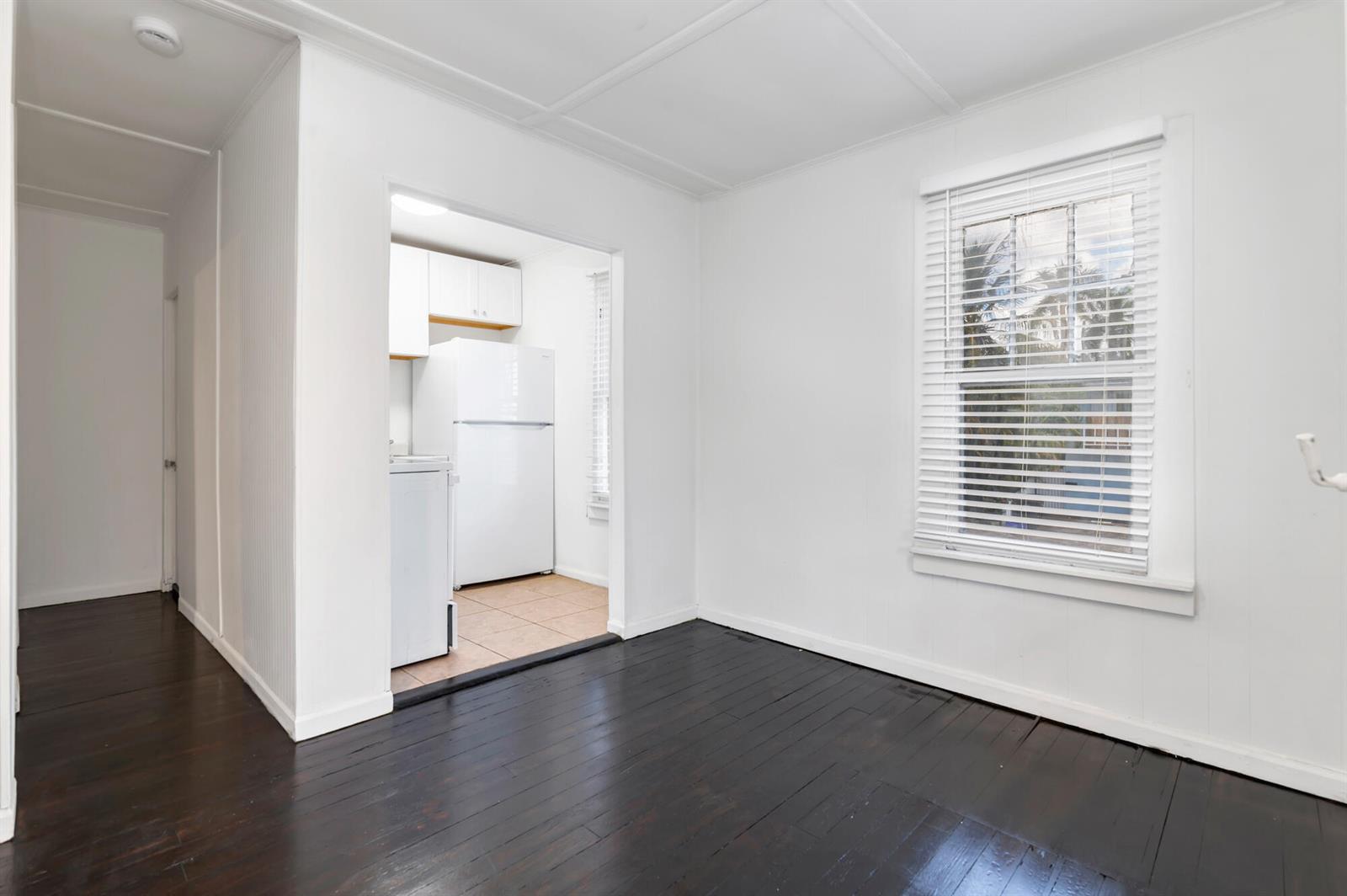 A room with dark wood floors and white walls leads to a small kitchen area — 204 Conniston Road, West Palm Beach FL 33405, WEST PALM BEACH, FL