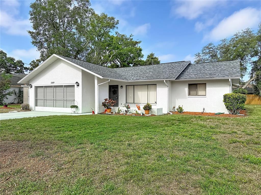 A single-story white house with a gray shingled roof and a front-facing garage — 5309 BAYONNE AVENUE, SPRING HILL, FL