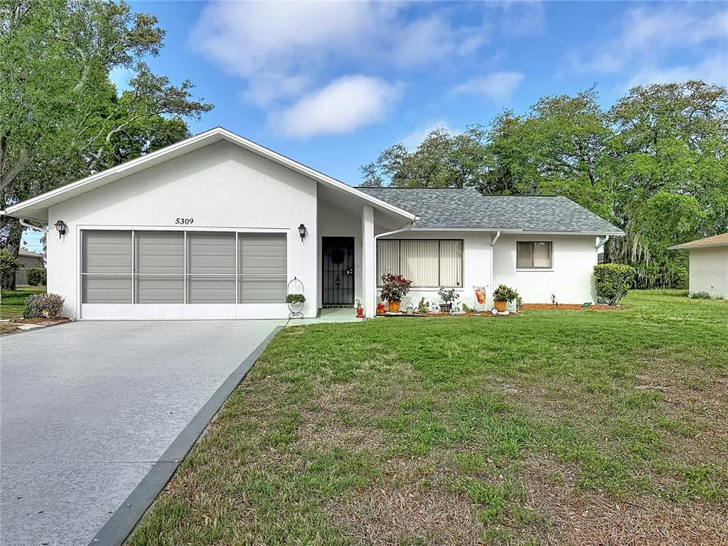 A single-story house with a white exterior, a screened garage, and a front lawn — 5309 BAYONNE AVENUE, SPRING HILL, FL