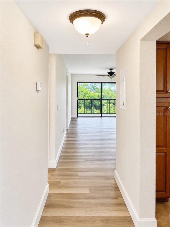 A hallway with light wood-look flooring leads toward a room with a balcony view — 1054 LOTUS COVE COURT UNIT 633, ALTAMONTE SPRINGS, FL