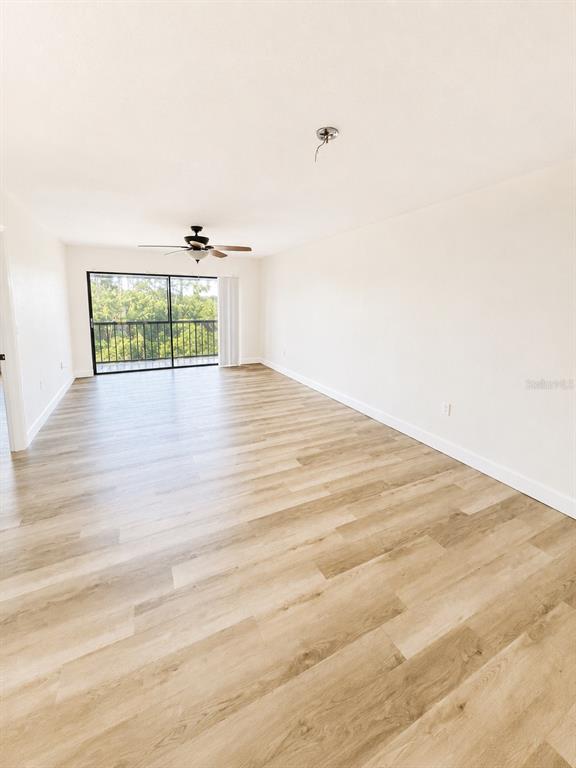 An empty living room features light wood-look flooring, a ceiling fan, and a sliding glass door — 1054 LOTUS COVE COURT UNIT 633, ALTAMONTE SPRINGS, FL