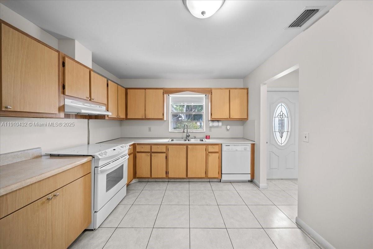A kitchen features light wood cabinets, white appliances, and light-colored tile flooring — 508 Holyoke Ln # A, Lake Worth FL 33467, LAKE WORTH, FL
