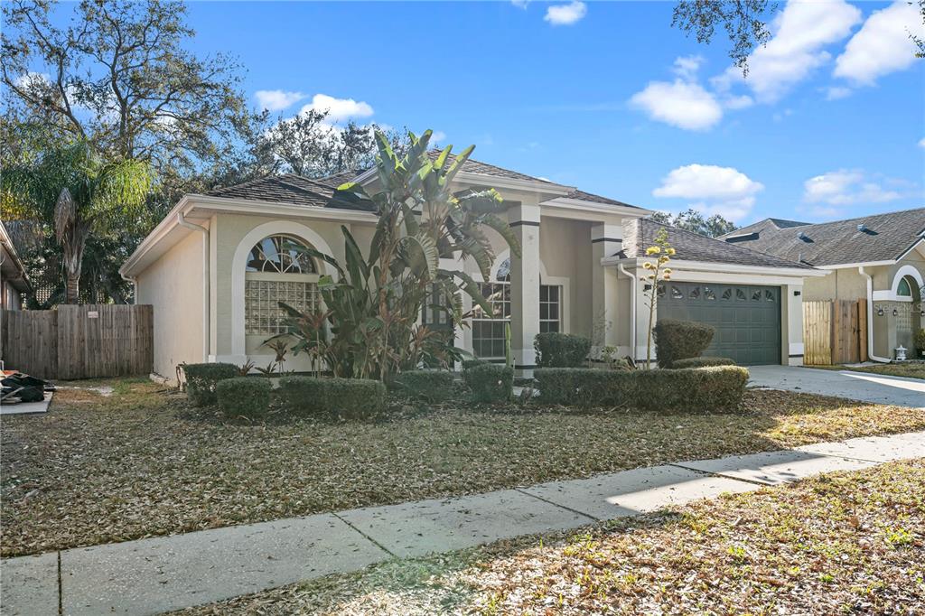 A single-story house with a beige exterior, a dark garage door, and a front yard — 3616 CYPRESS MEADOWS ROAD, TAMPA, FL