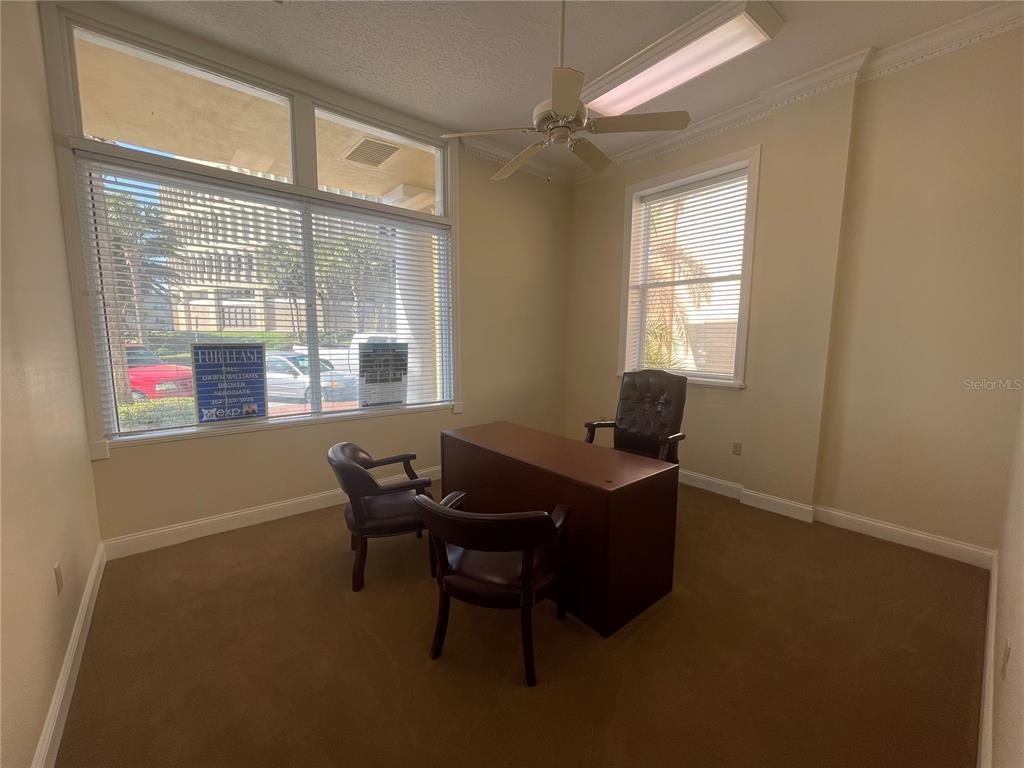 An office room features a desk, three chairs, large windows with blinds, and a ceiling fan — 220 W MAIN STREET, TAVARES, FL