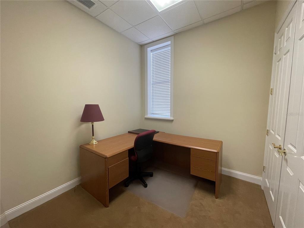 A small office features a wooden L-shaped desk, a rolling chair, and a table lamp — 220 W MAIN STREET, TAVARES, FL