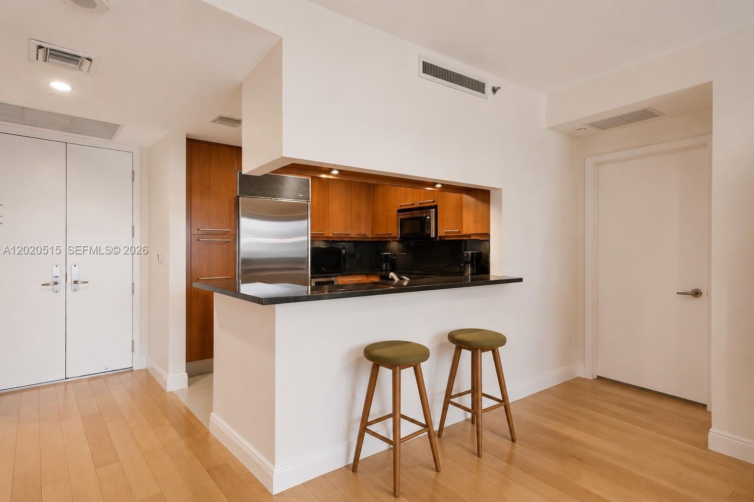 A kitchen with wood cabinets and a breakfast bar sits between two white doors — 901 Brickell Key Blvd # 609, Miami FL 33131, MIAMI, FL