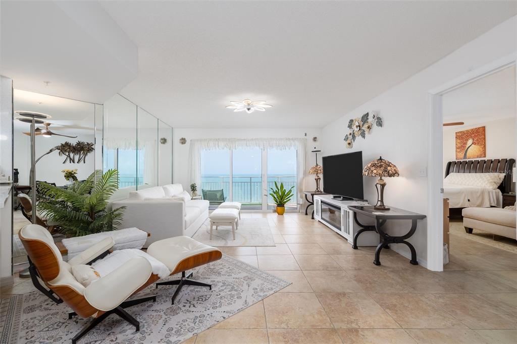 A living room with tile floors, a white sofa, a lounge chair, and a balcony view — 2967 S ATLANTIC AVENUE UNIT 1204, DAYTONA BEACH SHORES, FL