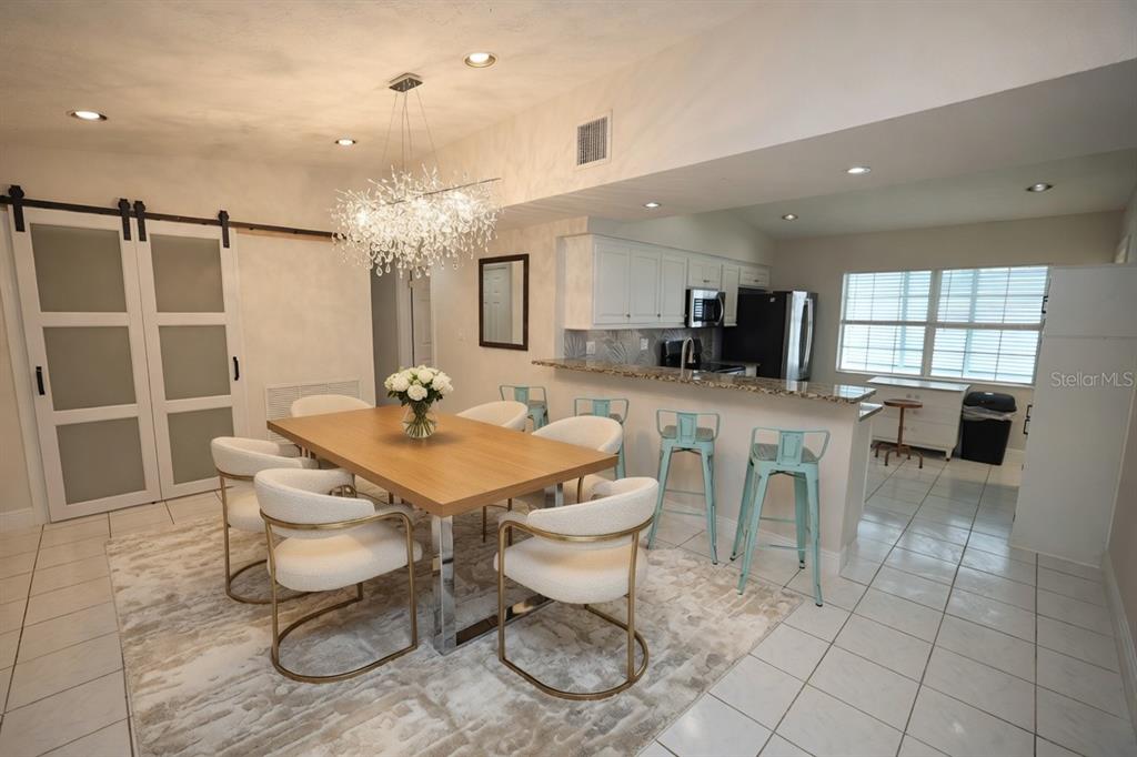 A dining area with a wooden table, white chairs, and a chandelier next to a kitchen — 3641 STOKES DRIVE, SARASOTA, FL