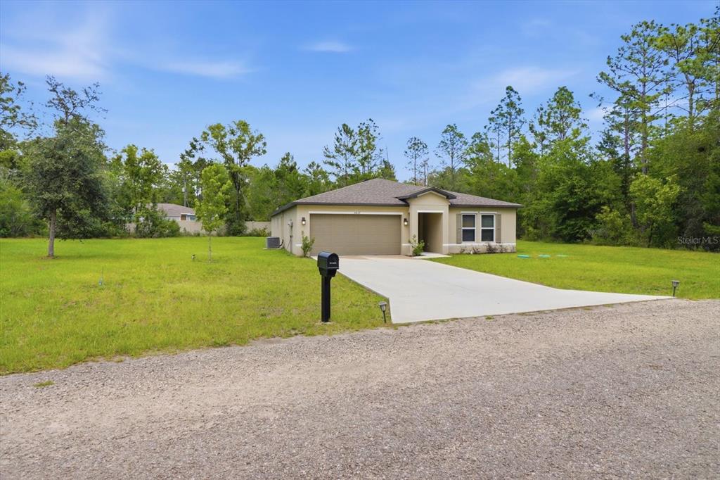 The exterior of a single-story home features a tan stucco facade, a garage, and entryway — 8827 N VIENNA DRIVE, DUNNELLON, FL