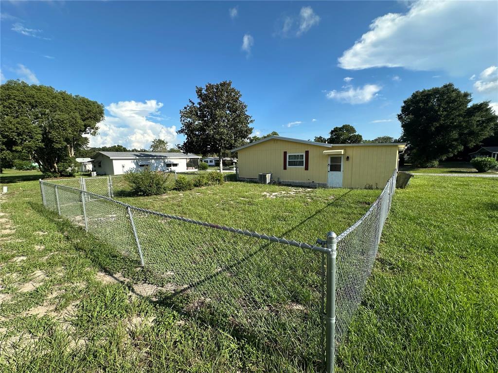 A yellow house with a chain-link fenced yard under a blue sky — 9050 SW 101 ST LANE, OCALA, FL