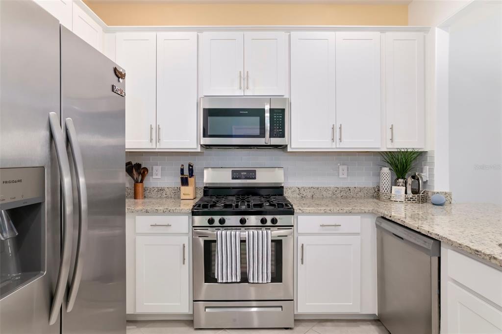 A kitchen featuring white cabinets, stainless steel appliances, and granite countertops with a tiled backsplash — 15030 SUNNY DAY DRIVE, BRADENTON, FL