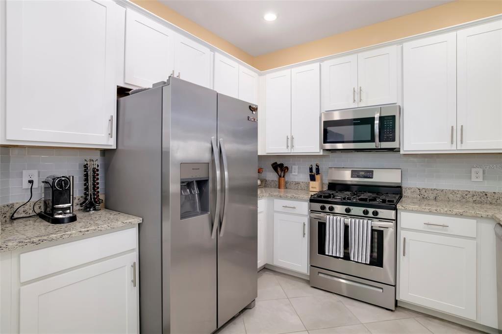 A kitchen features white cabinets, stainless steel appliances, granite countertops, and a light-colored tile floor — 15030 SUNNY DAY DRIVE, BRADENTON, FL