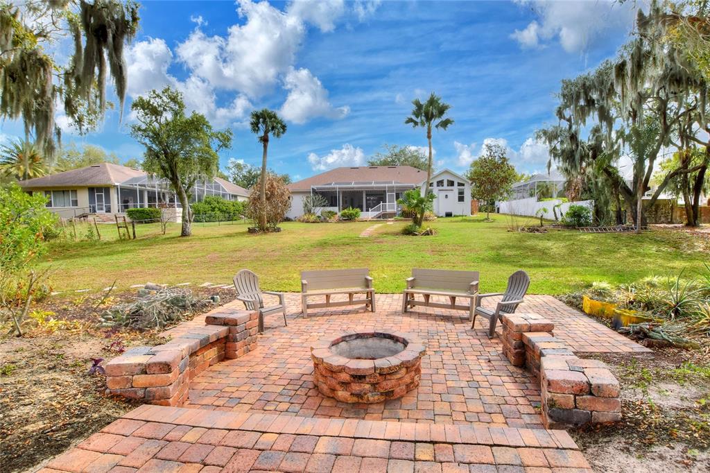 A brick patio with a fire pit and seating overlooks a large backyard and house — 858 HANOVER WAY, LAKELAND, FL