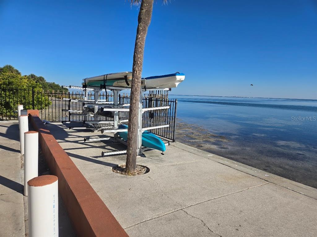A rack holding kayaks and paddleboards sits on a concrete walkway beside a bay — 650 PINELLAS POINT DRIVE S UNIT 204, ST PETERSBURG, FL