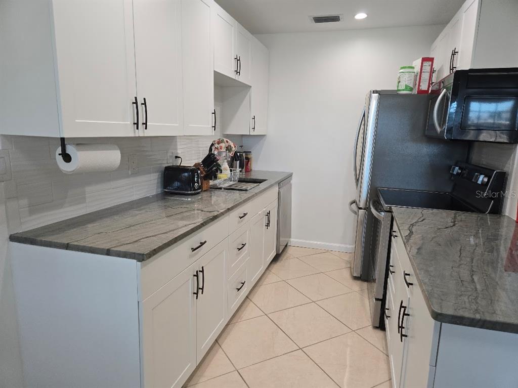A kitchen features white cabinets, gray stone countertops, stainless steel appliances, and tile flooring — 650 PINELLAS POINT DRIVE S UNIT 204, ST PETERSBURG, FL