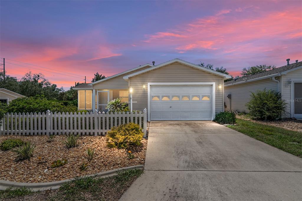 A single-story house with beige siding, a white garage door, and a white picket fence — 17300 SE 93RD HEYWARD AVENUE, THE VILLAGES, FL