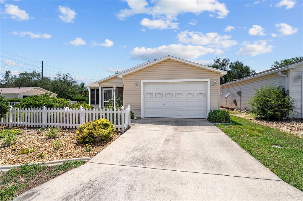 A single-story house with beige siding, a white garage door, and a white picket fence — 17300 SE 93RD HEYWARD AVENUE, THE VILLAGES, FL
