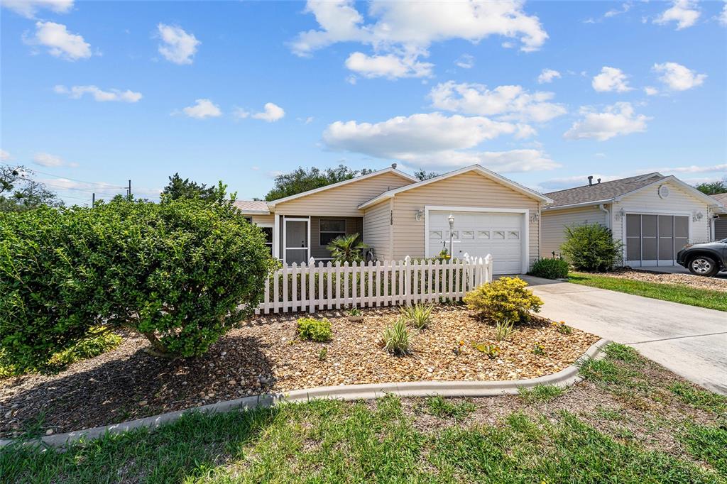 A single-story house with beige siding, a white picket fence, and a gravel front yard — 17300 SE 93RD HEYWARD AVENUE, THE VILLAGES, FL
