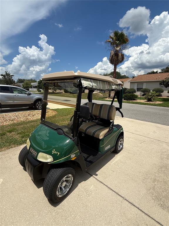 A green EZ-GO golf cart with striped seats is parked on a concrete driveway — 17300 SE 93RD HEYWARD AVENUE, THE VILLAGES, FL