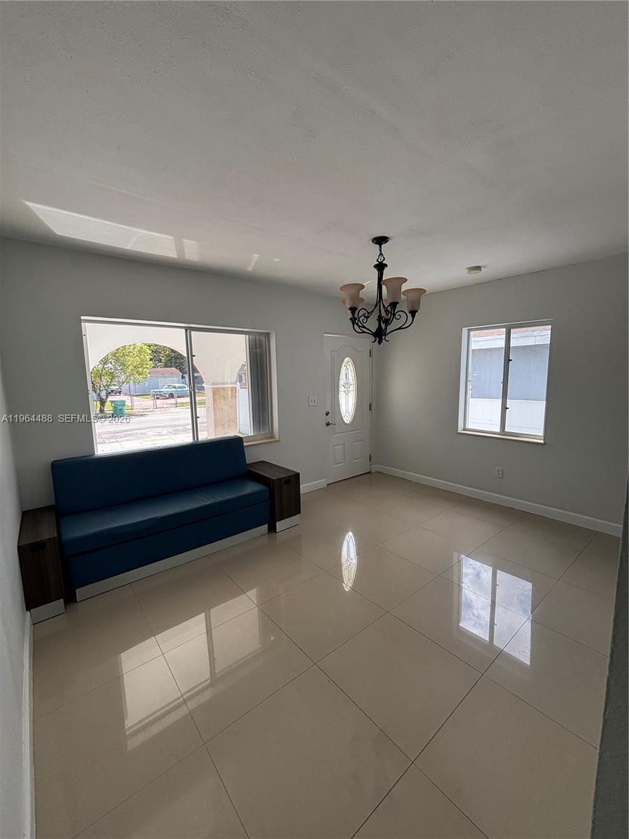 A living room features a blue sofa, tile flooring, a chandelier, and a front door — 6823 SW 25th St, Miami FL 33155, MIAMI, FL