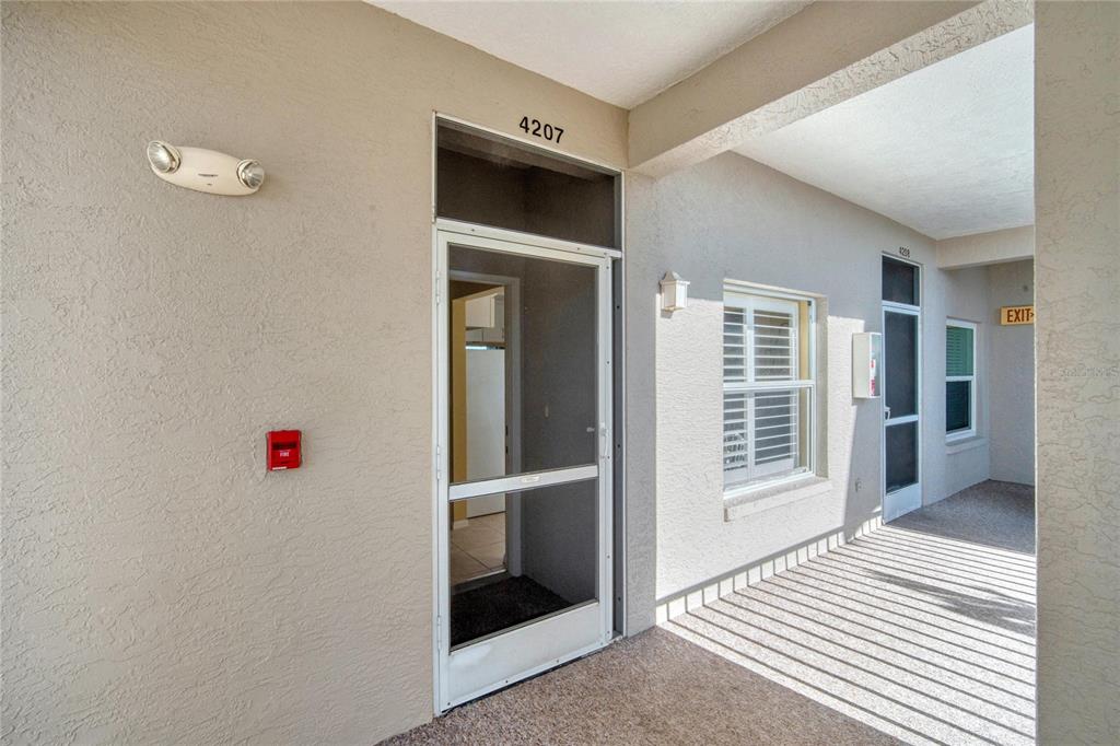 An exterior view of a building hallway showing apartment entry doors, a window, and lighting — 9610 CLUB SOUTH CIRCLE UNIT # 4207, SARASOTA, FL