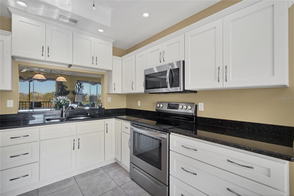 A kitchen features white cabinets, black countertops, stainless steel appliances, and a window view — 9610 CLUB SOUTH CIRCLE UNIT # 4207, SARASOTA, FL