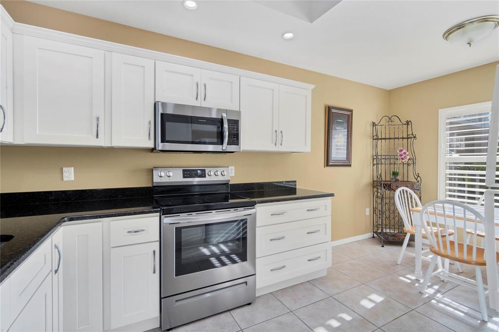 A kitchen with white cabinets, stainless steel appliances, black countertops, and a dining area — 9610 CLUB SOUTH CIRCLE UNIT # 4207, SARASOTA, FL