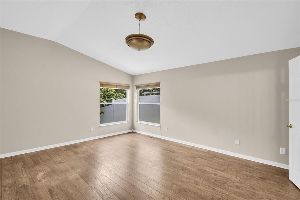 An empty room with light-colored walls, wood-look flooring, two windows, and a ceiling light fixture — 12415 RUSTIC VIEW COURT, TAMPA, FL