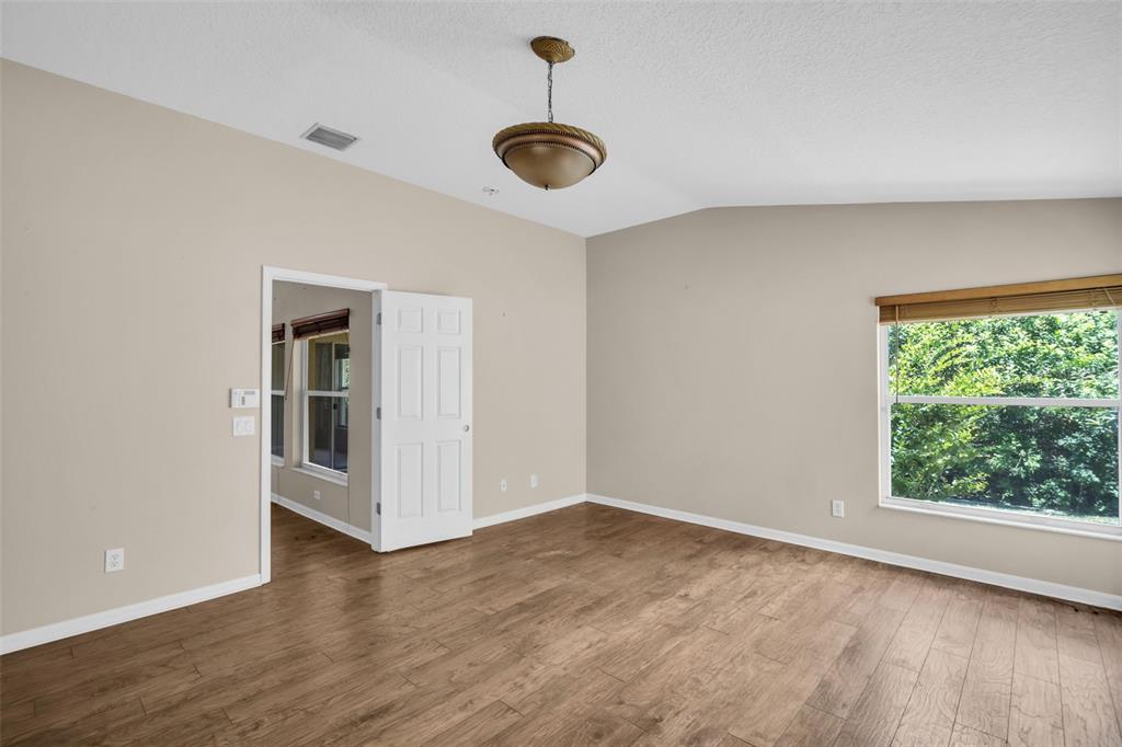 An empty room with light brown walls, wood-look flooring, a ceiling light, and a window — 12415 RUSTIC VIEW COURT, TAMPA, FL