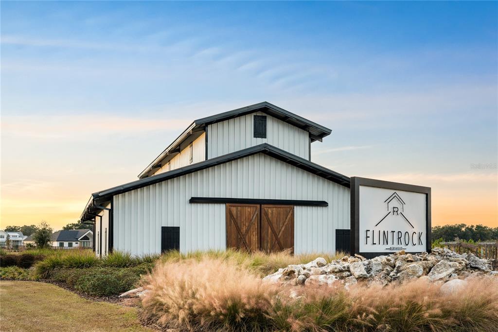 A white barn-style building with dark trim stands behind a sign labeled Flintrock Agrihood — Lot 39 SW 124TH WAY, ARCHER, FL