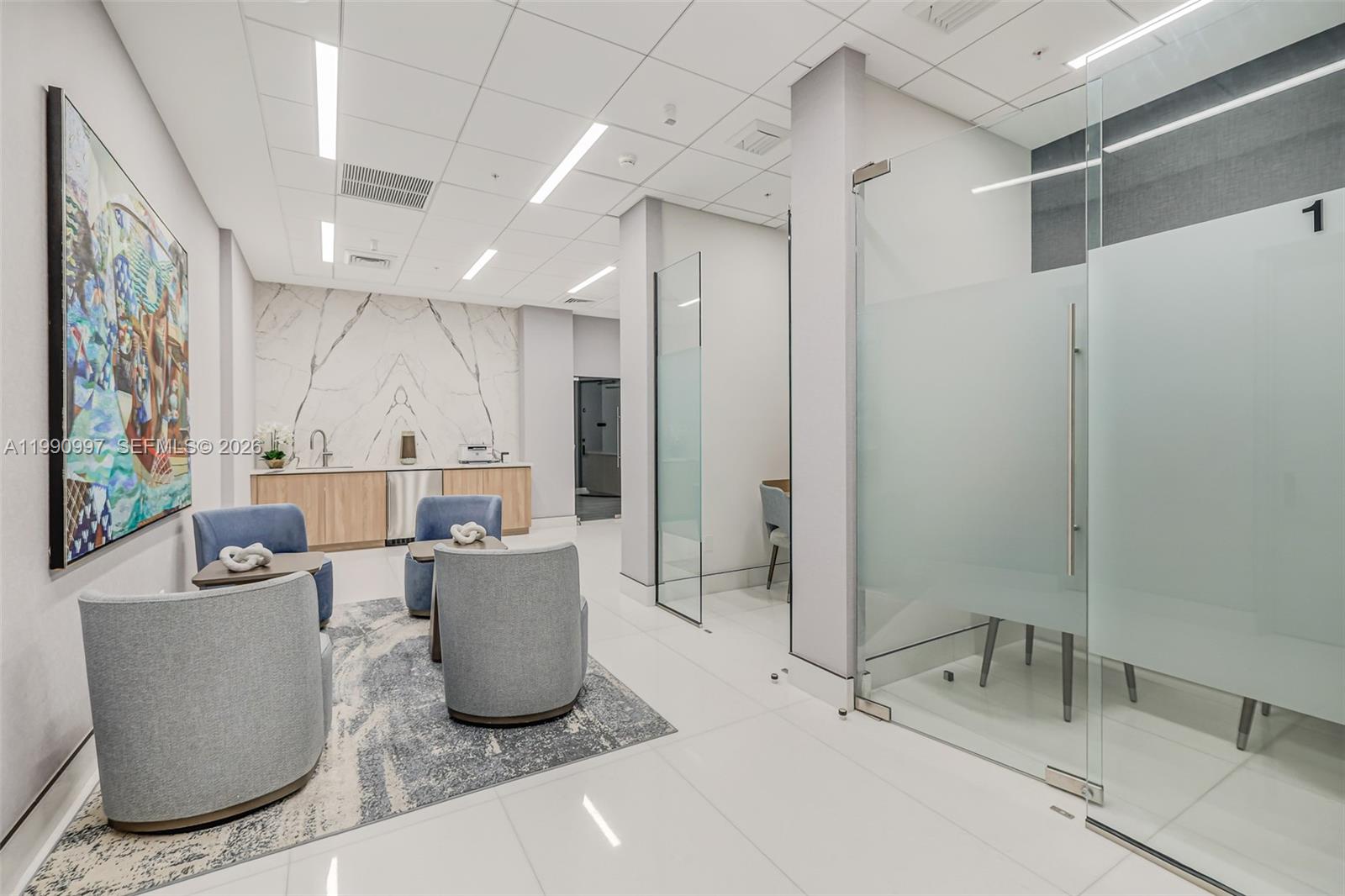 A modern office waiting area features blue armchairs, a marble accent wall, and glass-walled rooms — 888 Brickell Key Dr # 807, Miami FL 33131, MIAMI, FL