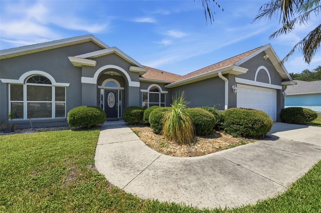A single-story gray house with a white garage, arched windows, and a curved concrete walkway — 36723 SUNDANCE DRIVE, GRAND ISLAND, FL