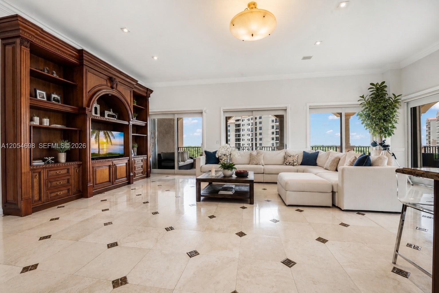 A spacious living room features a large wooden entertainment center, white sectional sofa, and tile flooring — 13633 Deering Bay Dr, Coral Gables FL 33158, CORAL GABLES, FL