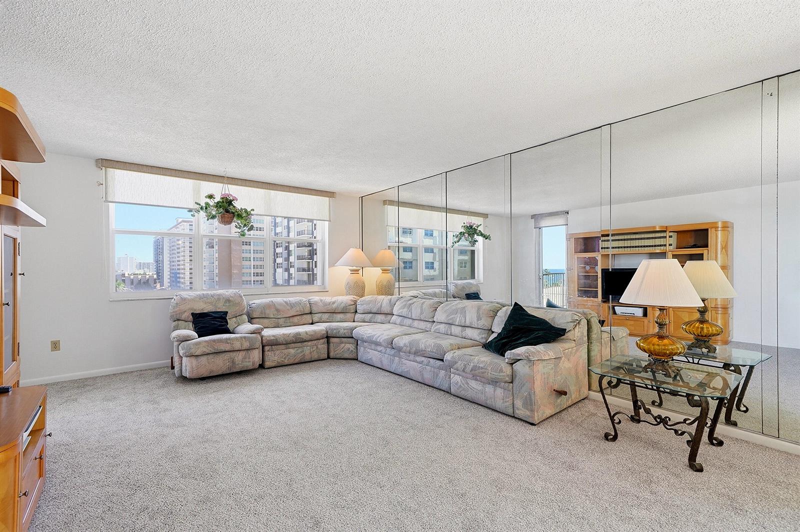 A living room features a large sectional sofa, mirrored walls, and a view of nearby buildings — 1401 S Ocean Drive # 704, Hollywood FL 33019, HOLLYWOOD, FL